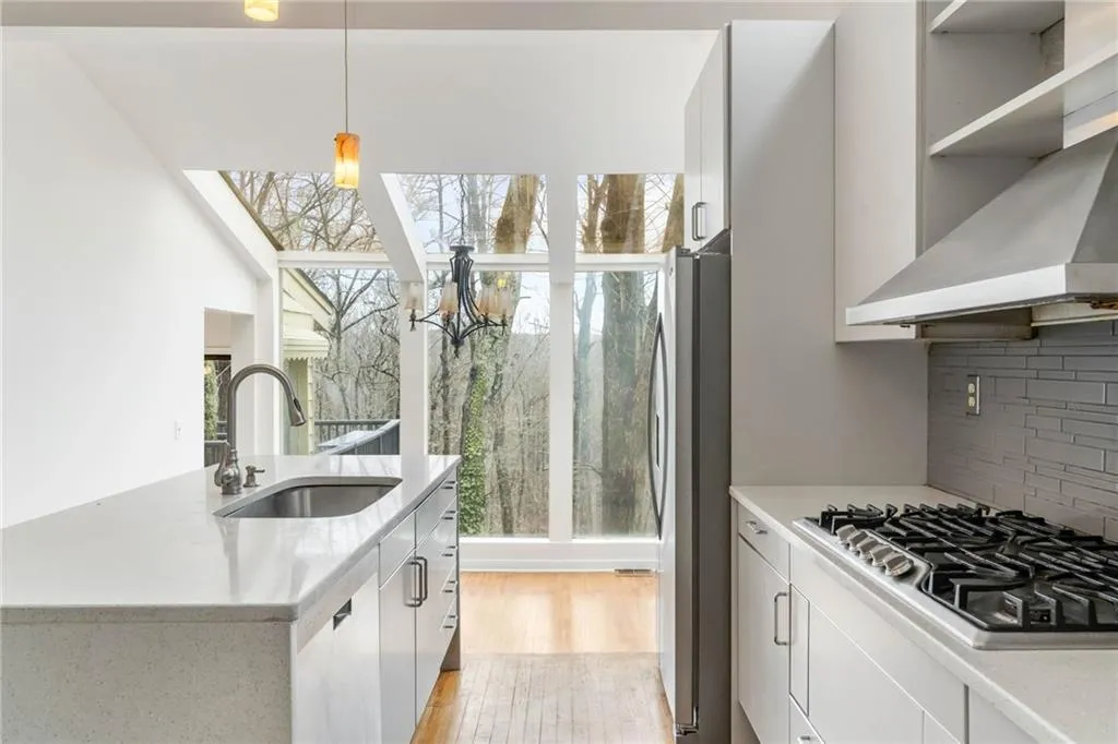 Kitchen featuring white cabinets, light wood-type flooring, decorative light fixtures, sink, and appliances with stainless steel finishes