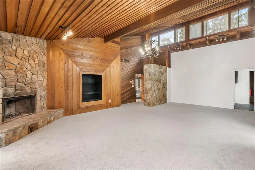 Unfurnished living room featuring wooden ceiling, wooden walls, a stone fireplace, carpet, and a notable chandelier