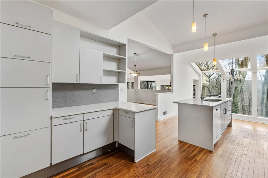 Kitchen with backsplash, hanging light fixtures, vaulted ceiling, dark hardwood / wood-style flooring, and white cabinetry