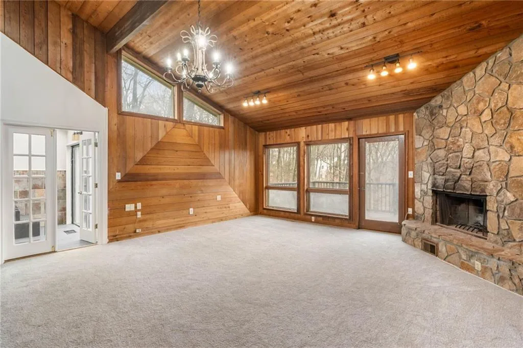Unfurnished living room featuring track lighting, wooden ceiling, a stone fireplace, light colored carpet, and a notable chandelier