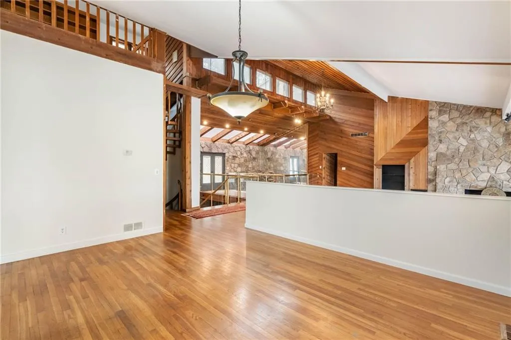 Unfurnished living room with high vaulted ceiling, light hardwood / wood-style flooring, beamed ceiling, and a notable chandelier
