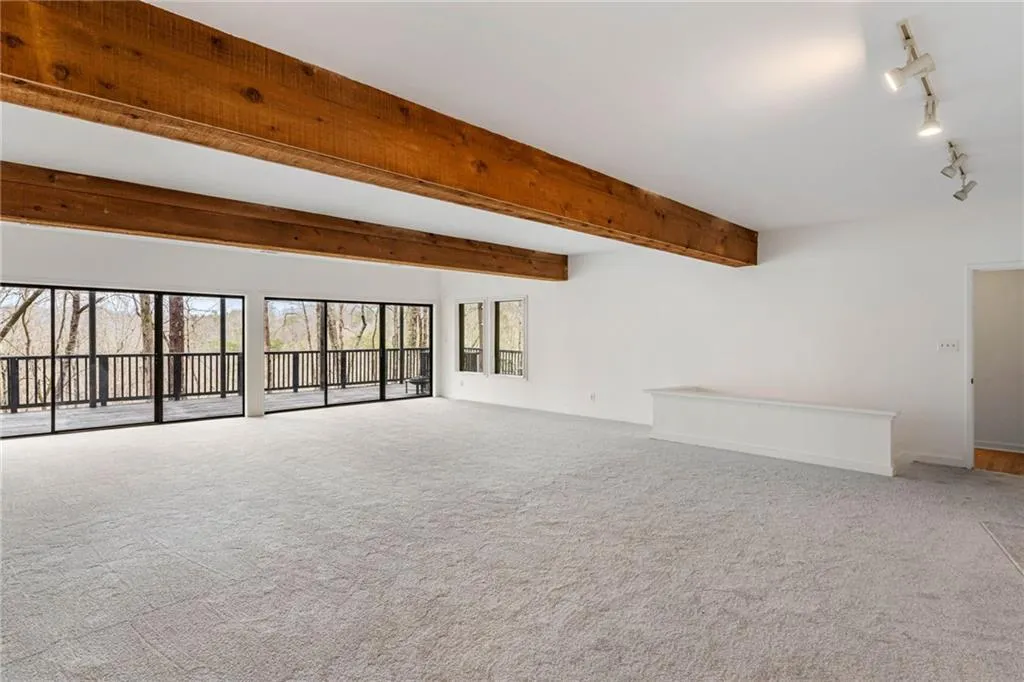 Unfurnished room featuring rail lighting, light carpet, and beamed ceiling