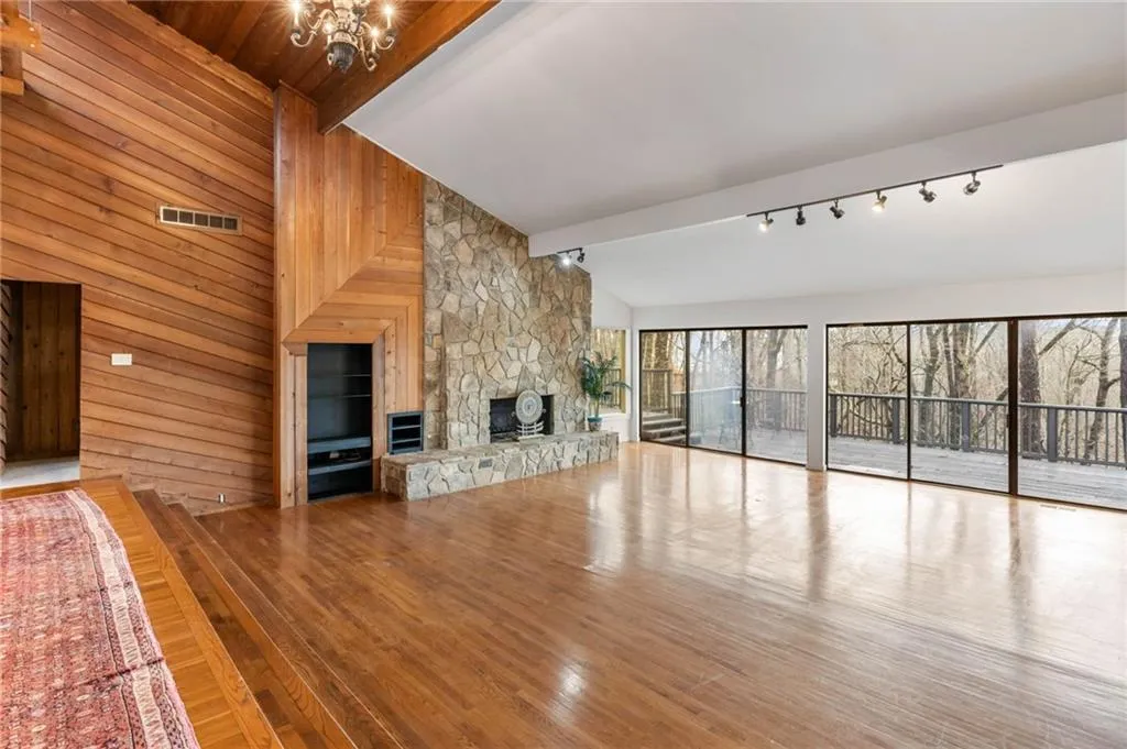Unfurnished living room featuring lofted ceiling with beams, light hardwood / wood-style floors, wood walls, and a fireplace