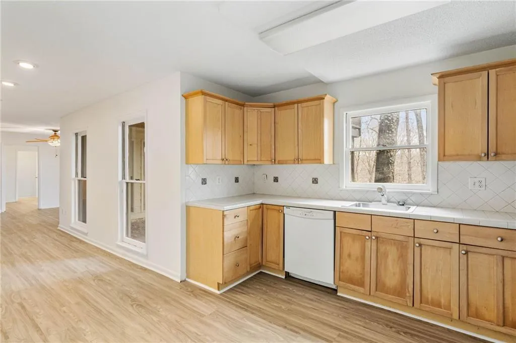 Kitchen featuring backsplash, sink, light wood-type flooring, ceiling fan, and dishwasher