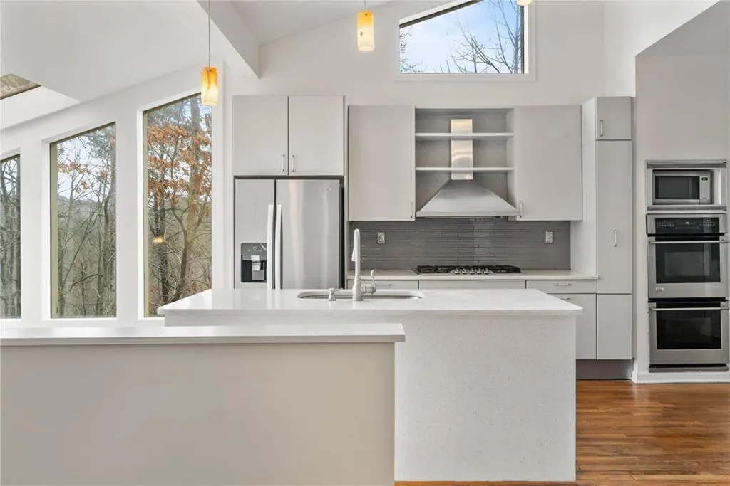 Kitchen featuring wall chimney range hood, pendant lighting, sink, vaulted ceiling, and appliances with stainless steel finishes