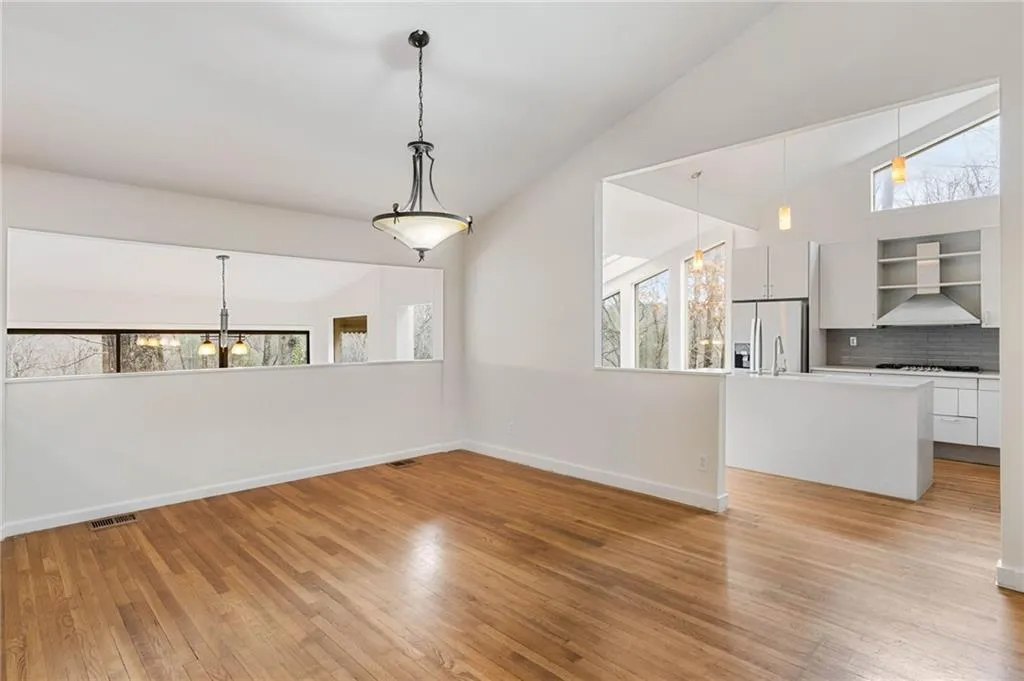 Unfurnished living room featuring a notable chandelier, lofted ceiling, a wealth of natural light, and light hardwood / wood-style floors