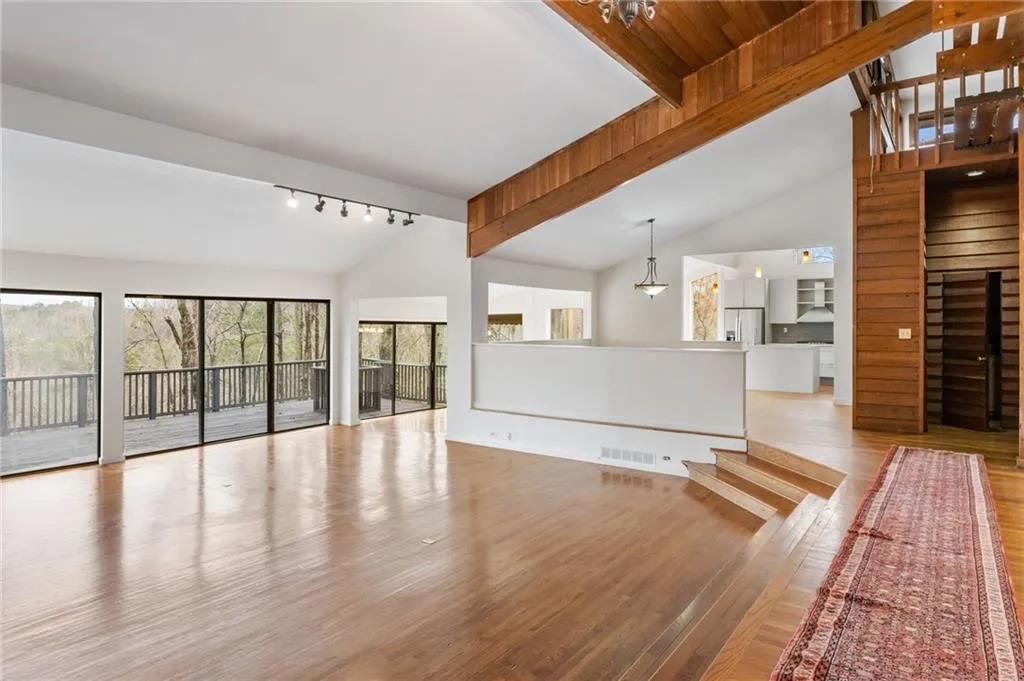 Unfurnished living room with an inviting chandelier, high vaulted ceiling, rail lighting, light wood-type flooring, and beamed ceiling