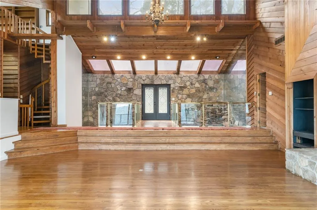 Unfurnished living room featuring french doors, an inviting chandelier, high vaulted ceiling, and light hardwood / wood-style floors