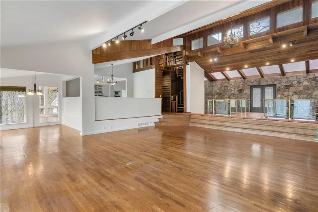 Unfurnished living room with an inviting chandelier, rail lighting, high vaulted ceiling, and light hardwood / wood-style floors