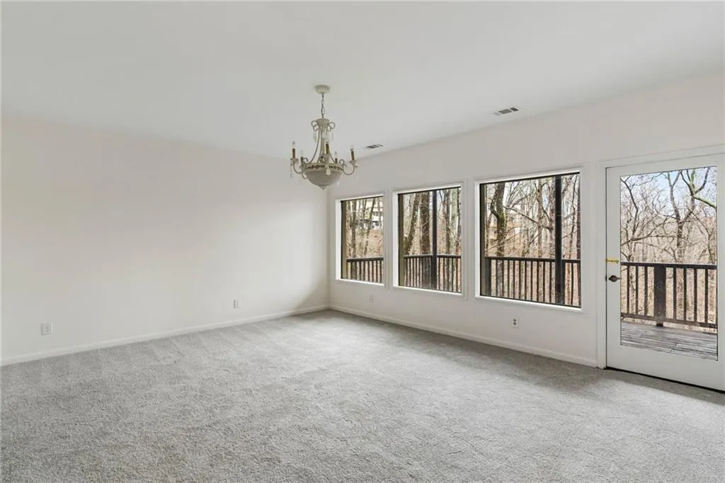 Spare room with light carpet, a wealth of natural light, and a chandelier