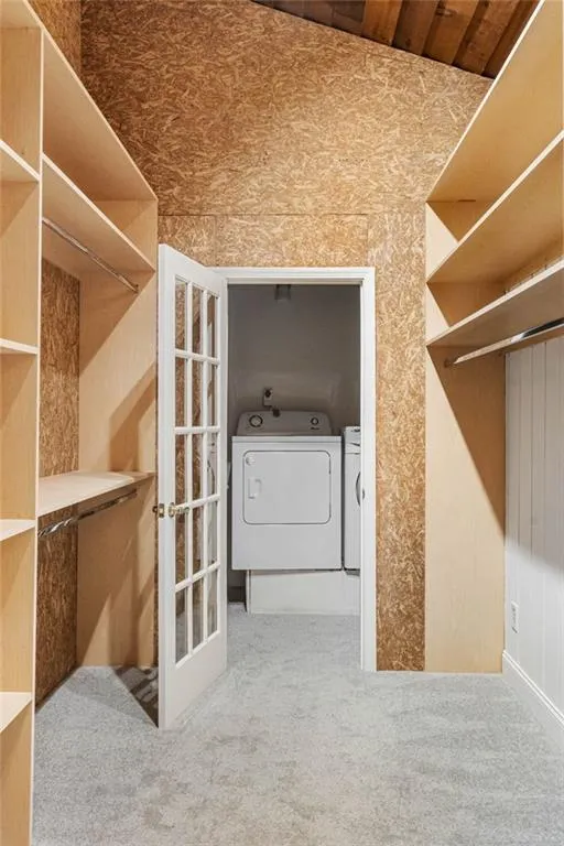 Walk in closet with light carpet and washing machine and clothes dryer