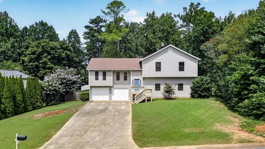 Split-level residence featuring a two-car garage, front yard landscaping, and mature surrounding trees