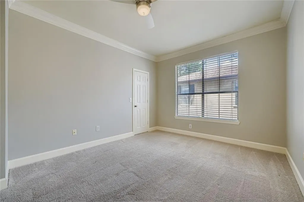 Empty room featuring light colored carpet, ornamental molding, and a ceiling fan