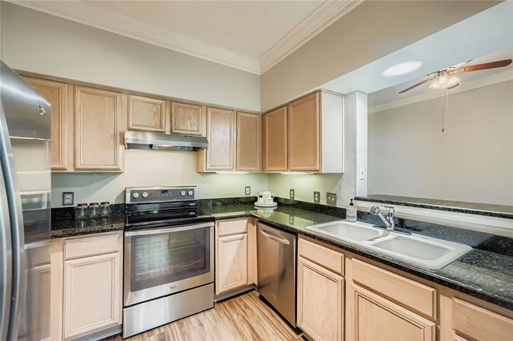 Kitchen with ornamental molding, appliances with stainless steel finishes, light brown cabinetry, light wood-type flooring, and under cabinet range hood