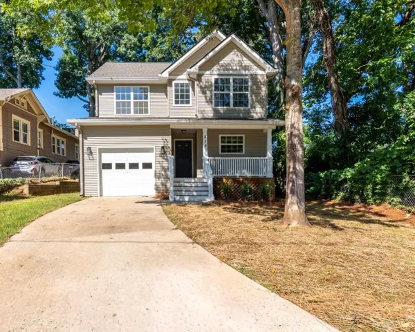 Two-story property featuring horizontal siding, a covered front porch with white railings, an attached garage, a paved driveway, and mature trees