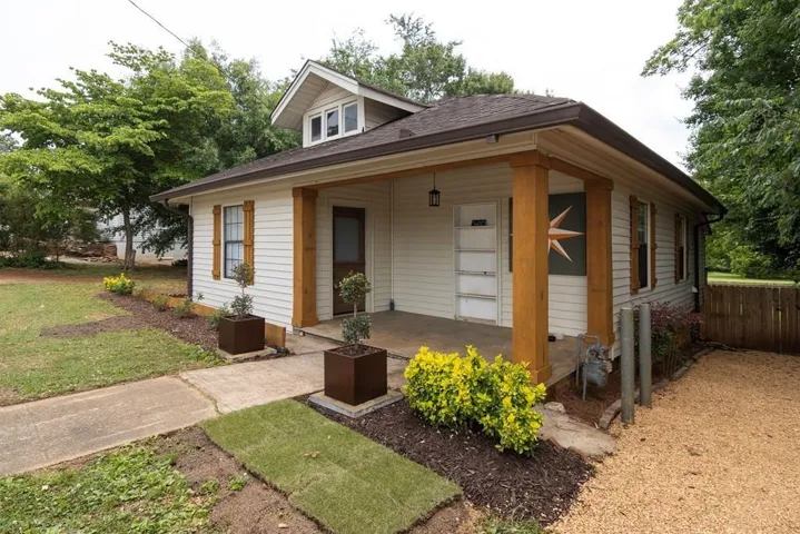 White siding exterior with a brown shingle roof and a covered front porch featuring two substantial wood-toned posts