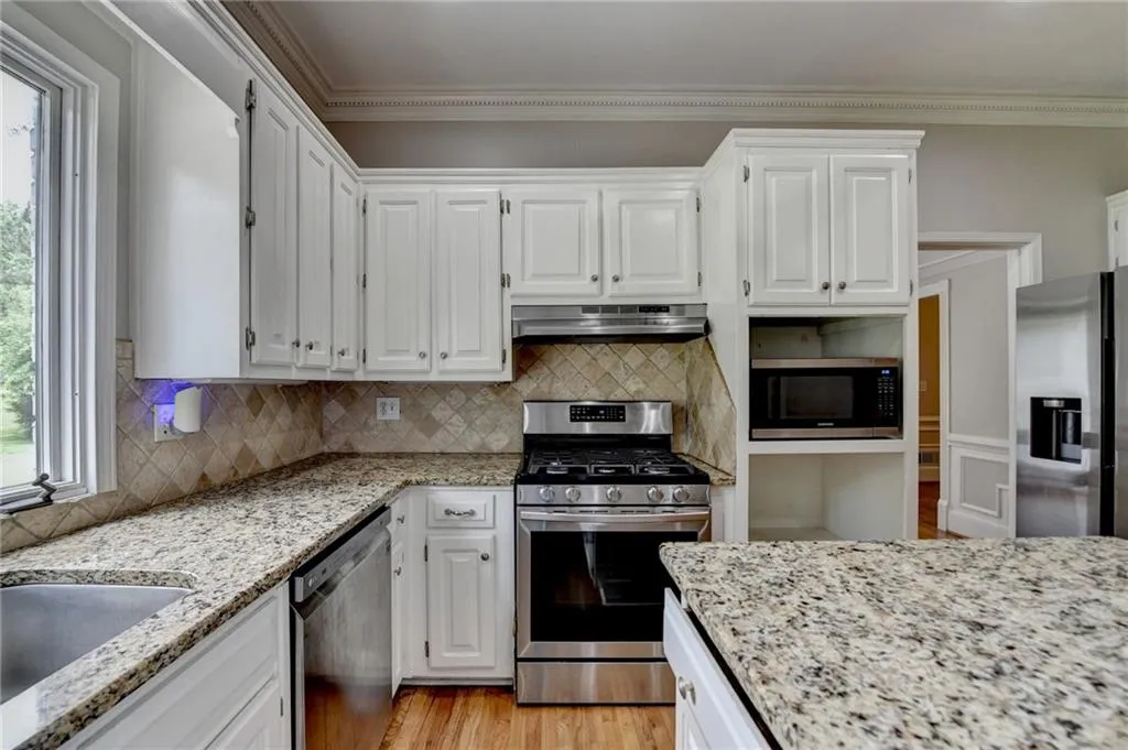 Kitchen with stainless steel appliances, under cabinet range hood, white cabinets, and crown molding