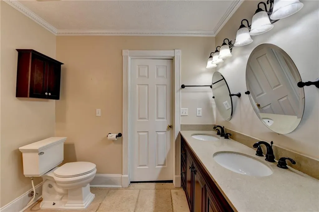 Bathroom featuring baseboards, crown molding, toilet, double vanity, and tile patterned flooring
