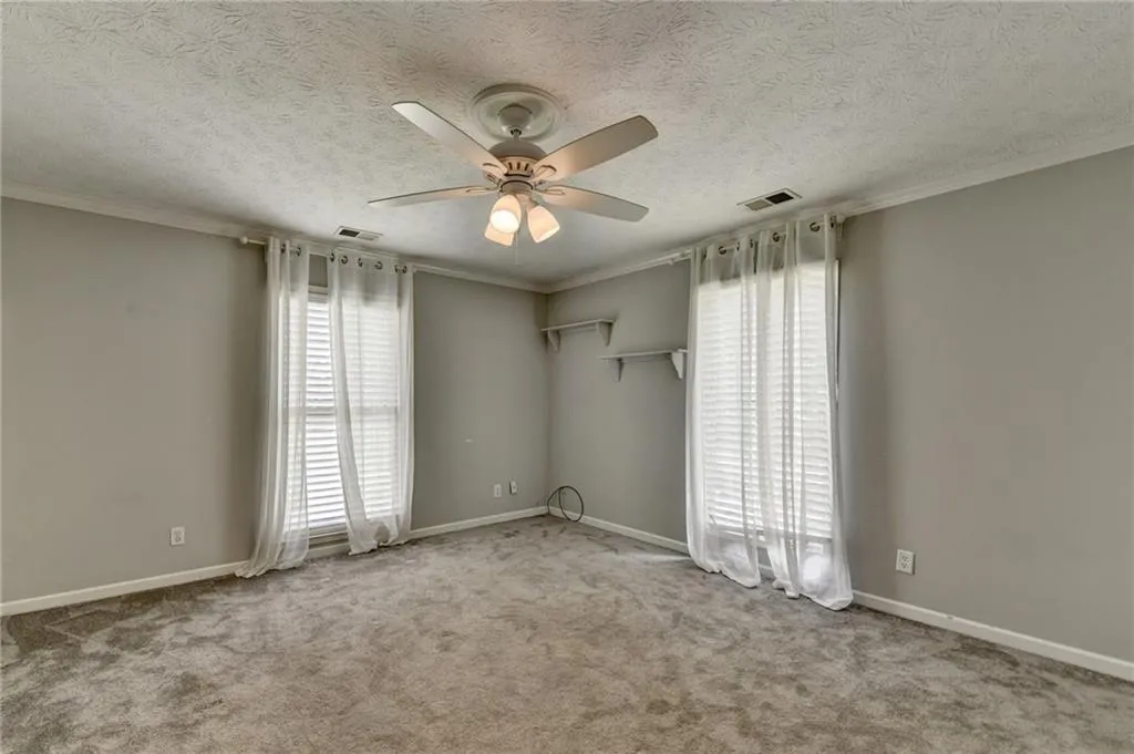 Carpeted spare room featuring healthy amount of natural light, a ceiling fan, baseboards, ornamental molding, and a textured ceiling
