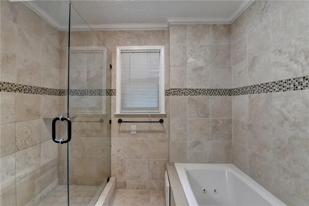 Bathroom with ornamental molding, a shower stall, a jetted tub, and tile walls