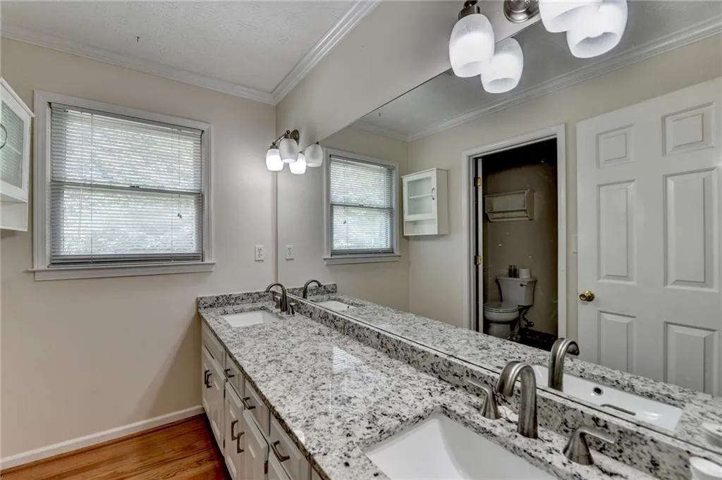 Full bath with wood finished floors, toilet, baseboards, double vanity, and ornamental molding