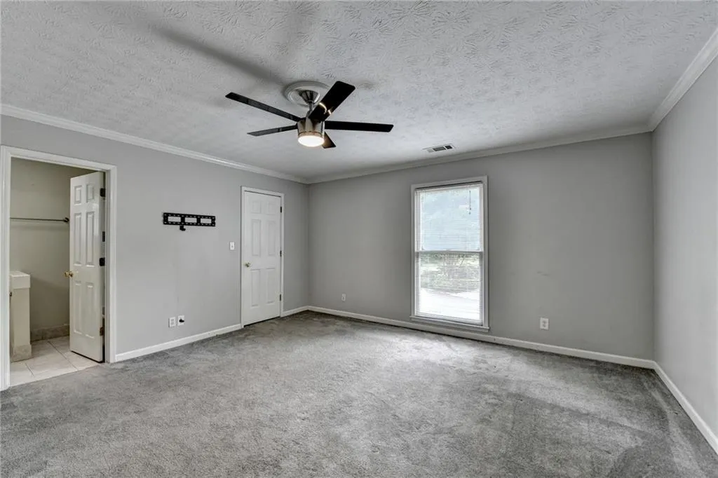 Unfurnished bedroom featuring carpet floors, ornamental molding, baseboards, ensuite bath, and ceiling fan