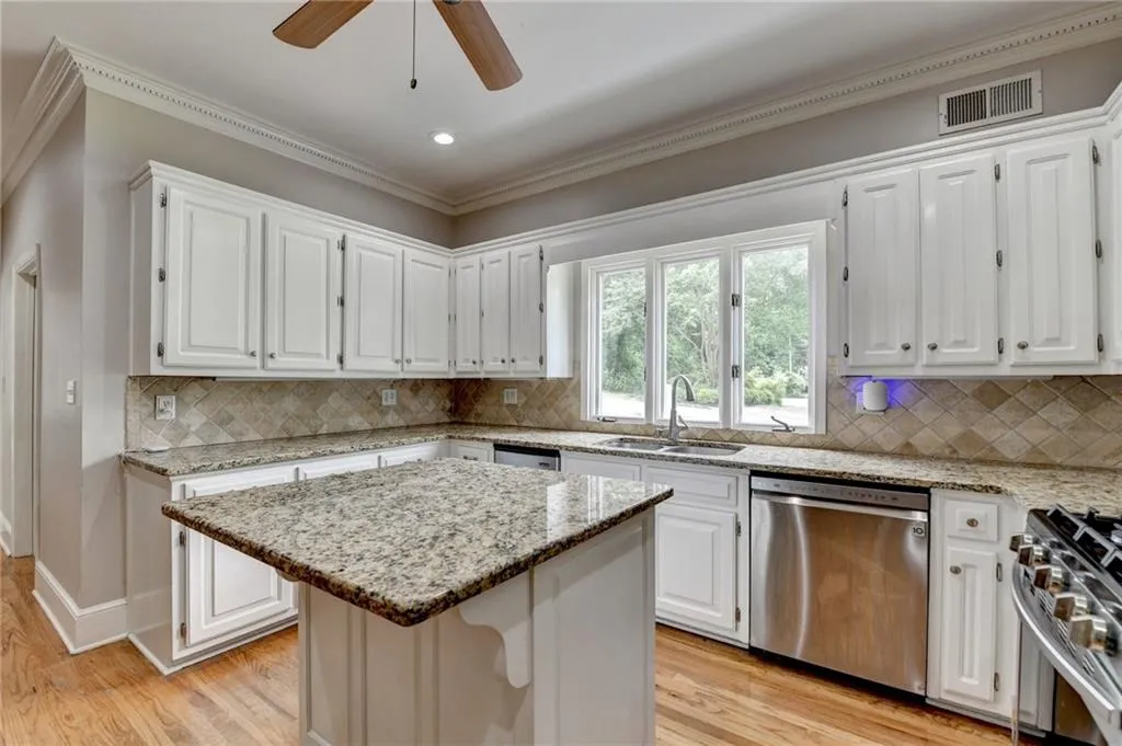 Kitchen with stainless steel appliances, a sink, light wood-style flooring, a center island, and white cabinetry
