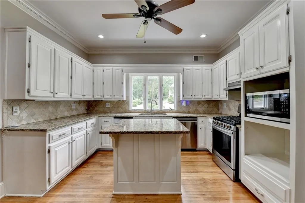 Kitchen featuring stainless steel appliances, white cabinets, a sink, a center island, and light stone counters
