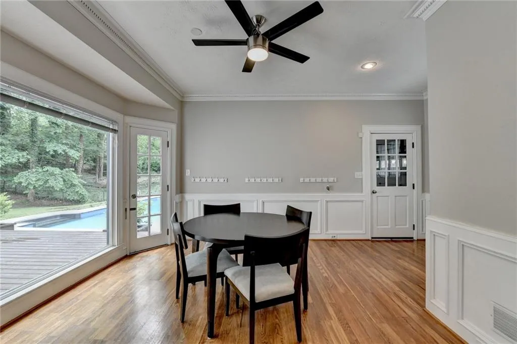 Dining area with crown molding, ceiling fan, a decorative wall, light wood-style floors, and wainscoting