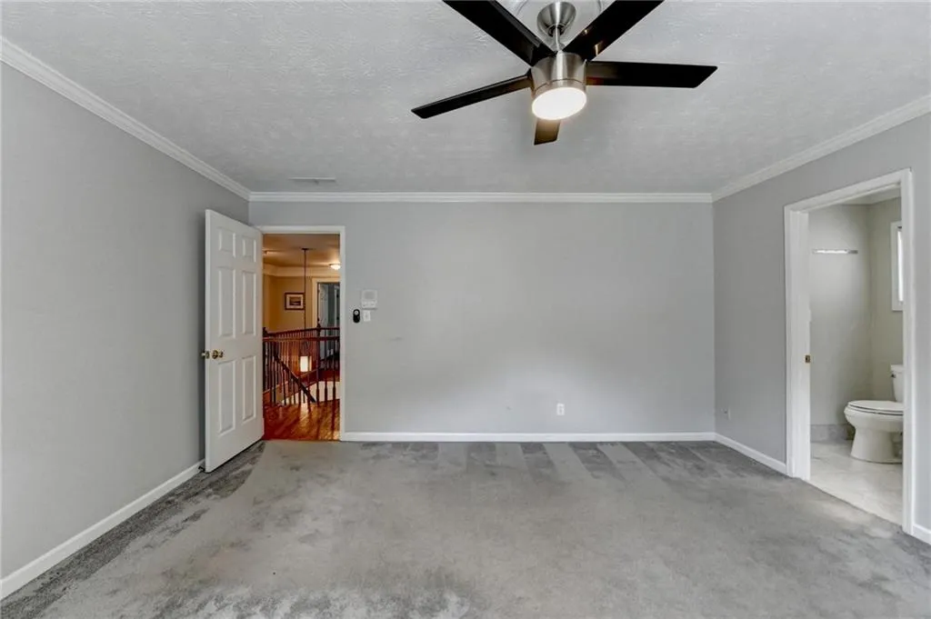 Unfurnished bedroom featuring carpet flooring, baseboards, crown molding, a textured ceiling, and connected bathroom