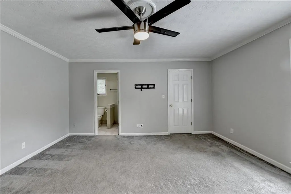 Unfurnished bedroom with ornamental molding, carpet, a textured ceiling, baseboards, and ensuite bathroom