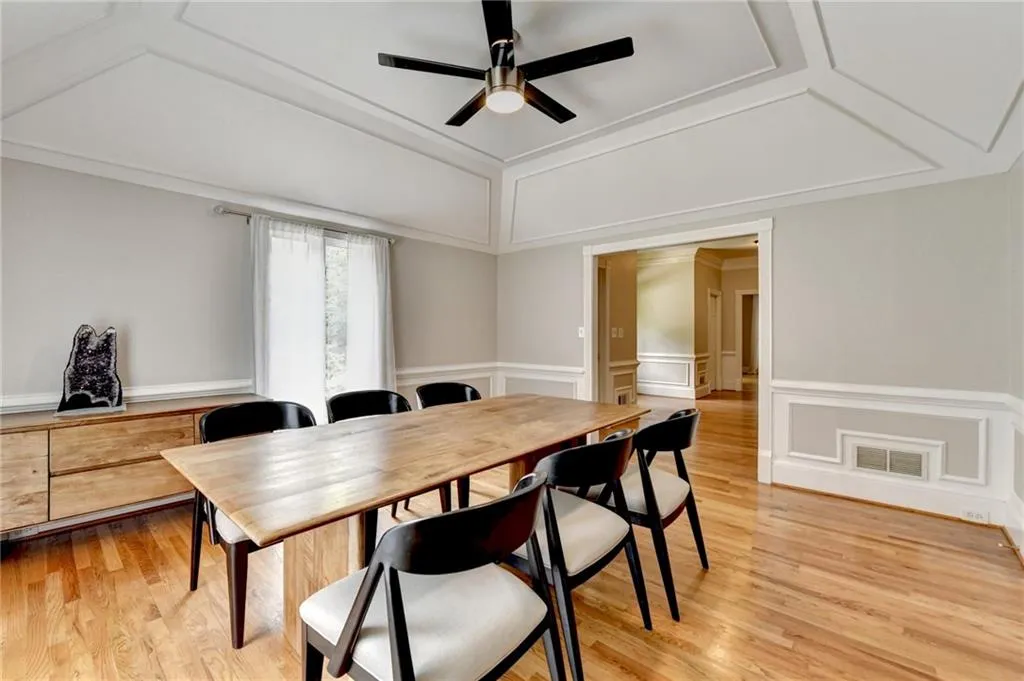 Dining room featuring ceiling fan, lofted ceiling, light wood-style flooring, a wainscoted wall, and a decorative wall