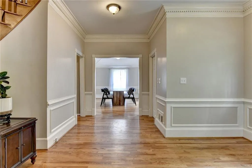 Hallway featuring light wood finished floors, ornamental molding, a wainscoted wall, a decorative wall, and stairs