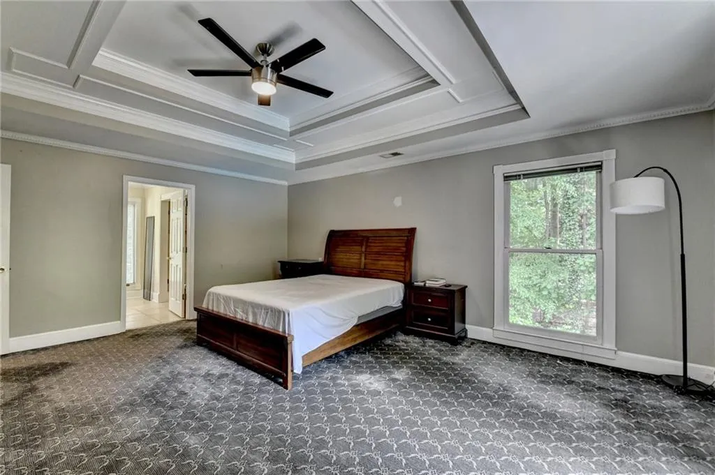 Bedroom with ornamental molding, carpet, a raised ceiling, baseboards, and ceiling fan
