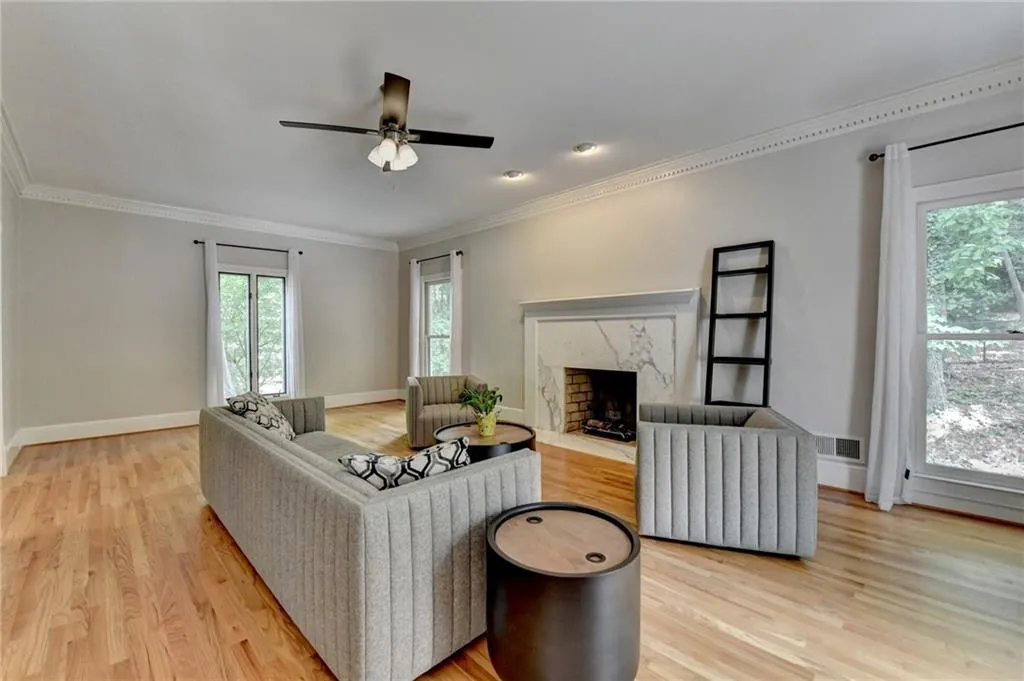 Living room featuring light wood-type flooring, crown molding, a premium fireplace, baseboards, and a ceiling fan