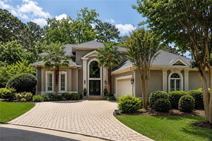 Stucco exterior residence featuring a curved paver driveway, two palm trees, arched entry with double doors, and an integrated garage