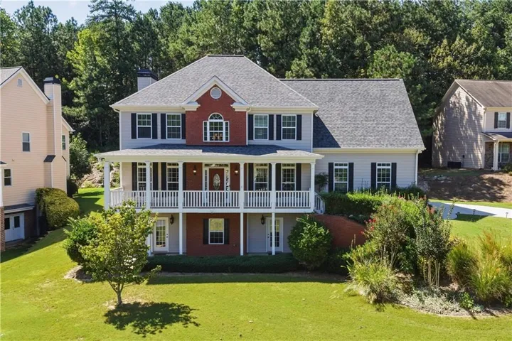 Two-story residence featuring a covered front porch with white railings, a red brick facade accent, and dark shutters