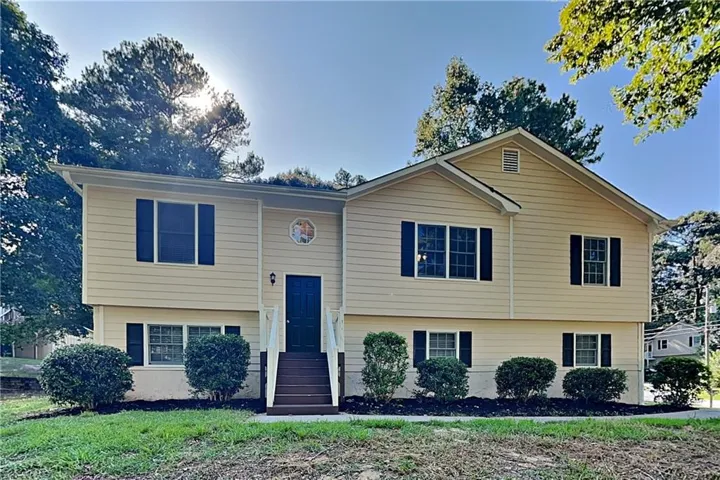 Split-level residence featuring light-colored siding, dark shutters, and a dark entry door