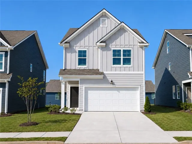 Light gray vertical and horizontal siding with white trim, attached two-car garage, dark entry door, concrete driveway, and green lawn