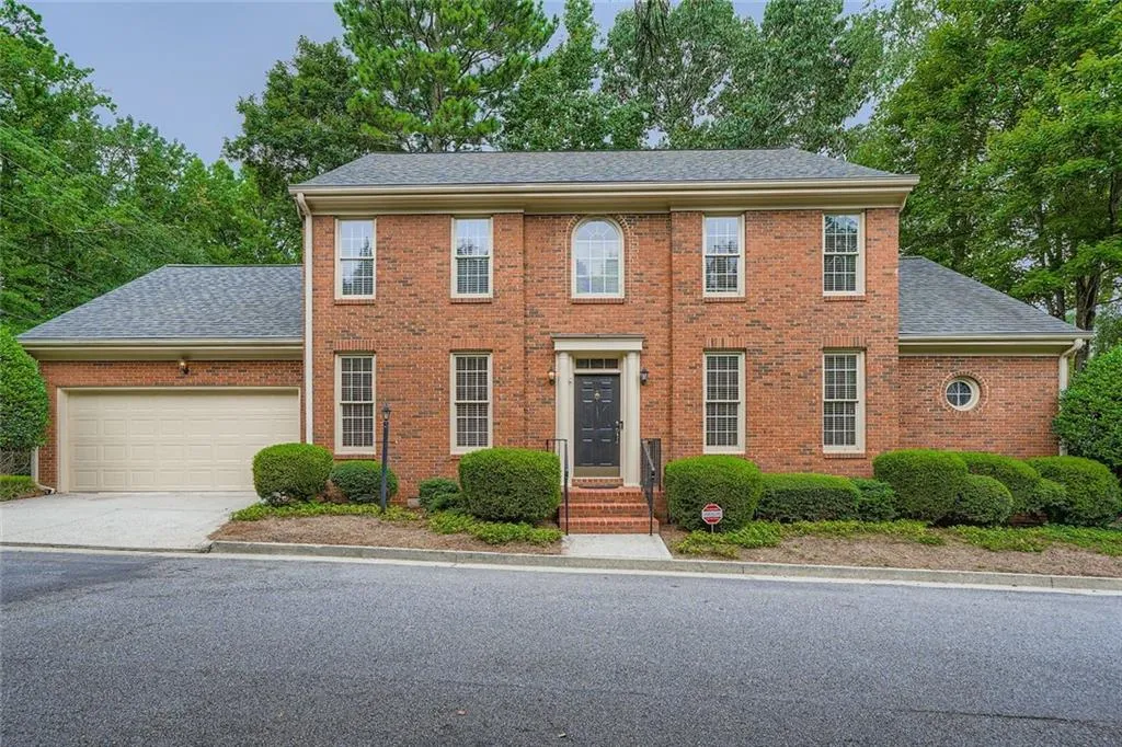 Colonial inspired home with a garage, roof with shingles, concrete driveway, and brick siding