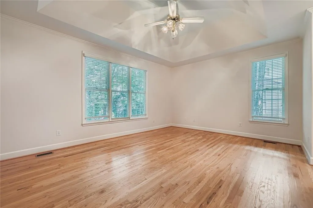 Spare room with a raised ceiling, light wood finished floors, crown molding, and a ceiling fan