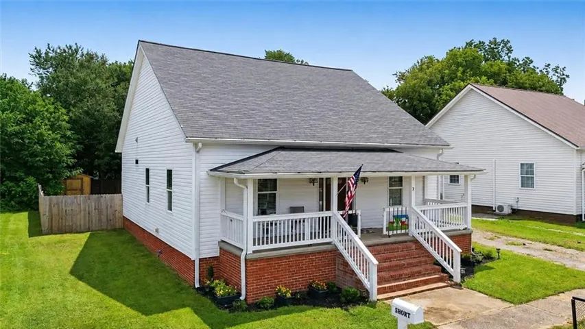 White siding exterior with a shingle roof, covered front porch, and brick foundation