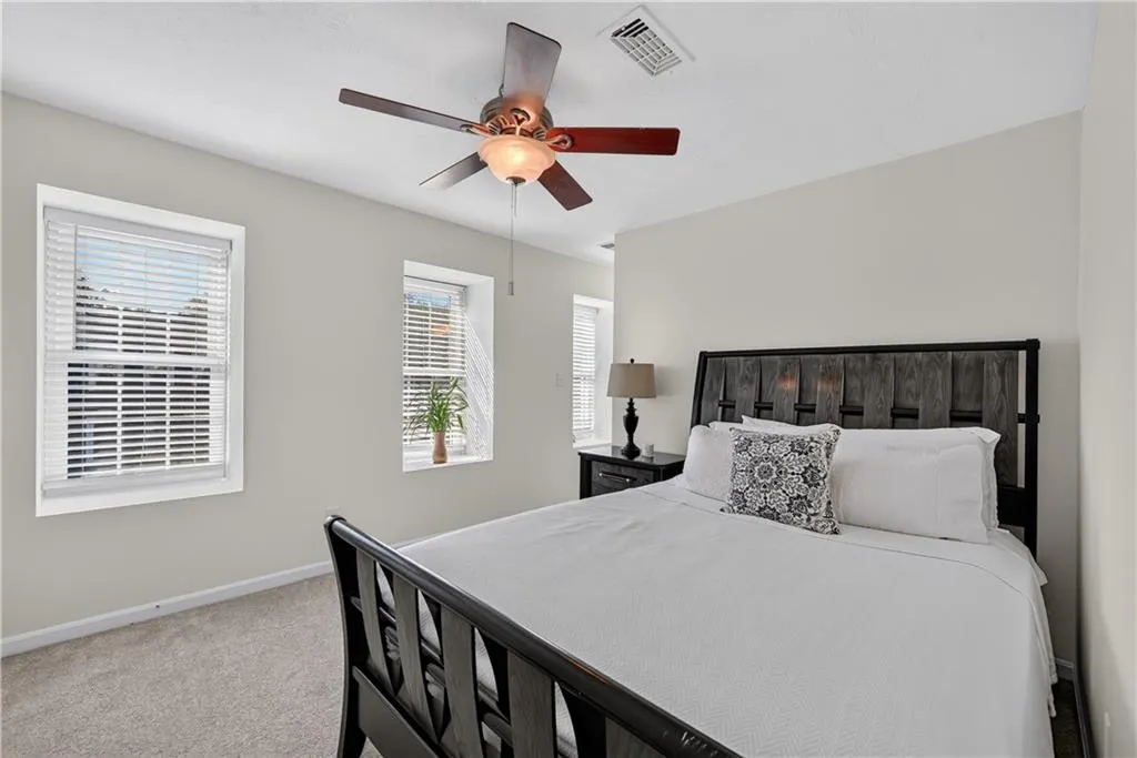 Neutral-toned walls, ceiling-mounted paddle fan with integrated lighting, wall-to-wall carpeting, and multiple windows with horizontal blinds