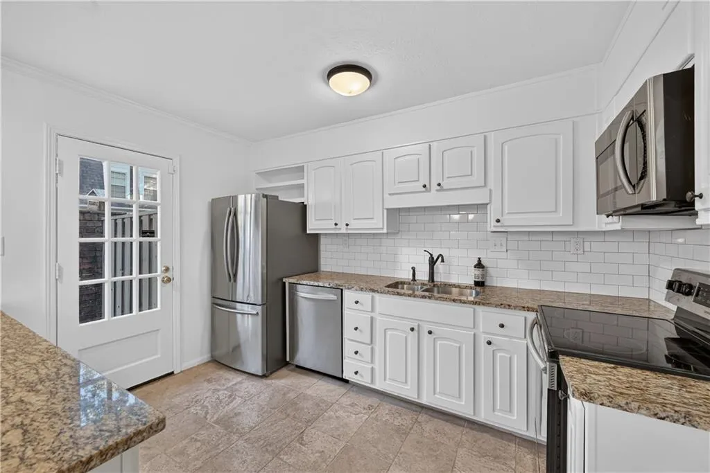 Kitchen featuring white cabinetry, stone-finish countertops, subway tile backsplash, stainless steel appliances, and a glass-paneled exterior door