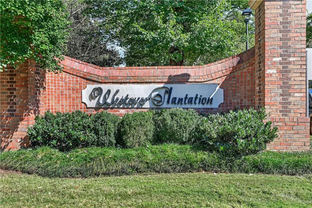 Curved red brick monument sign with integrated signage and decorative post-top lighting, surrounded by manicured shrubbery and lawn landscaping