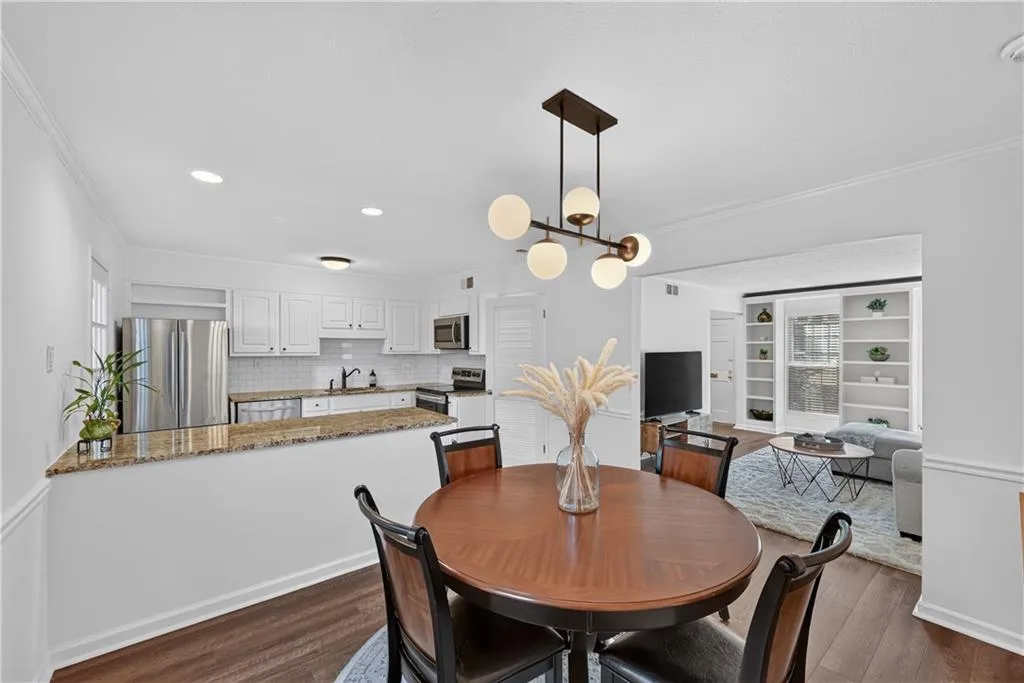 Dining area featuring wood-finish flooring, a contemporary multi-light fixture, and a kitchen peninsula with stone-finish countertops and white cabinetry