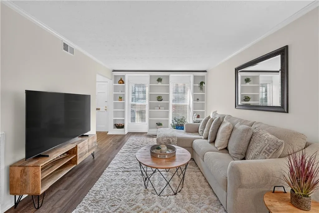 Neutral-toned living space featuring wood-finish flooring, floor-to-ceiling built-in white shelving, and crown molding