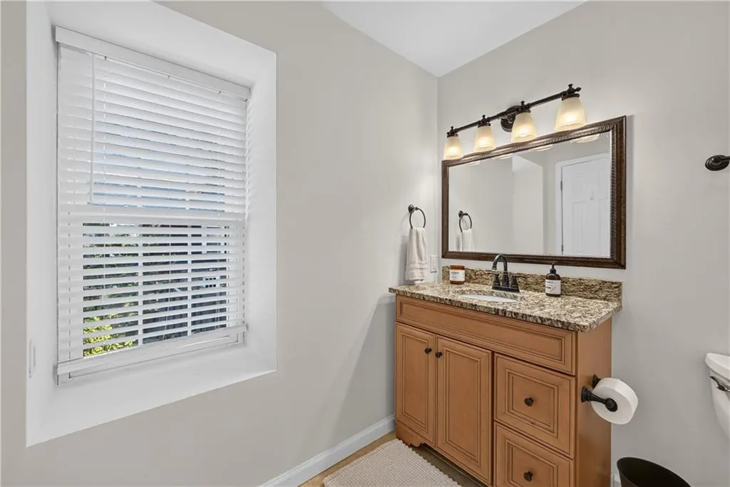 Bathroom vanity featuring a natural wood-finish cabinet, stone-finish countertop, under-mount sink with a matte black faucet, and a wall-mounted light fixture with frosted glass shades