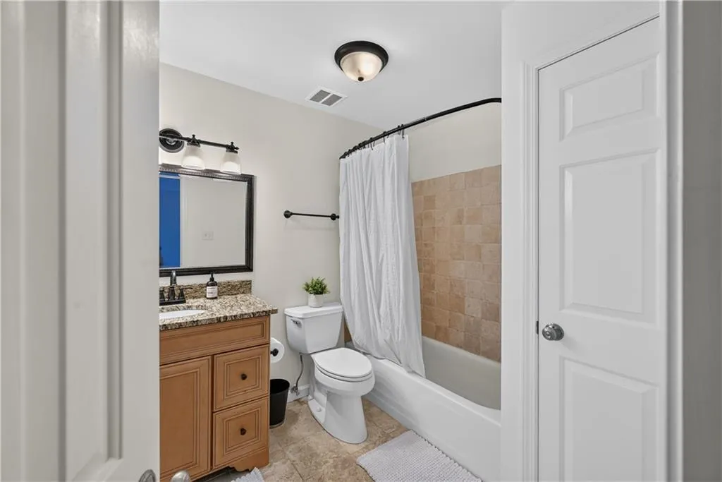 Bathroom featuring a wood-finish vanity with a stone countertop, an integrated sink with a dark-finish faucet, a framed vanity mirror, and a tub-shower combination with tile surround