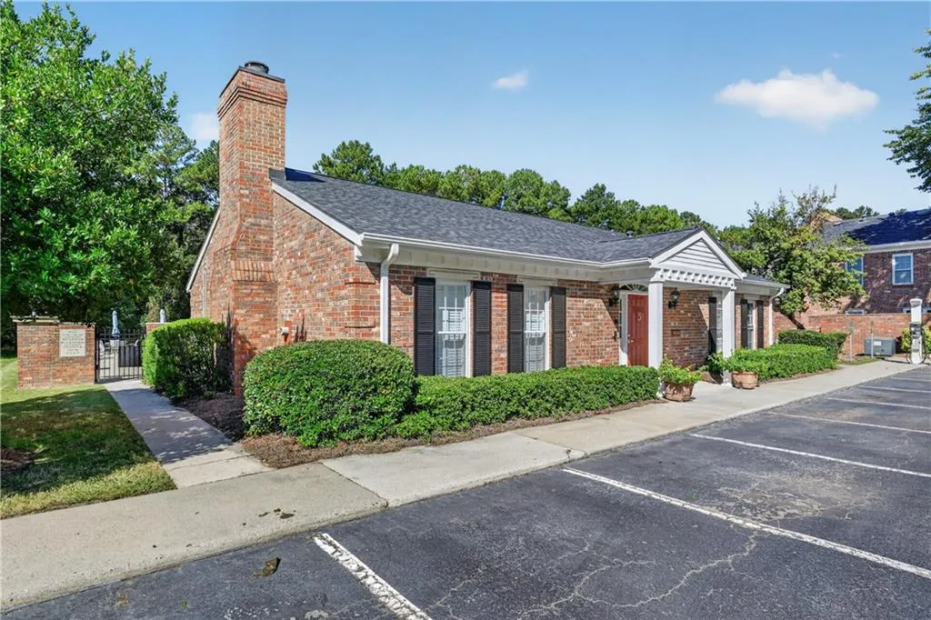 Brick exterior featuring a masonry chimney, shuttered windows, a pedimented entryway, and asphalt shingle roofing